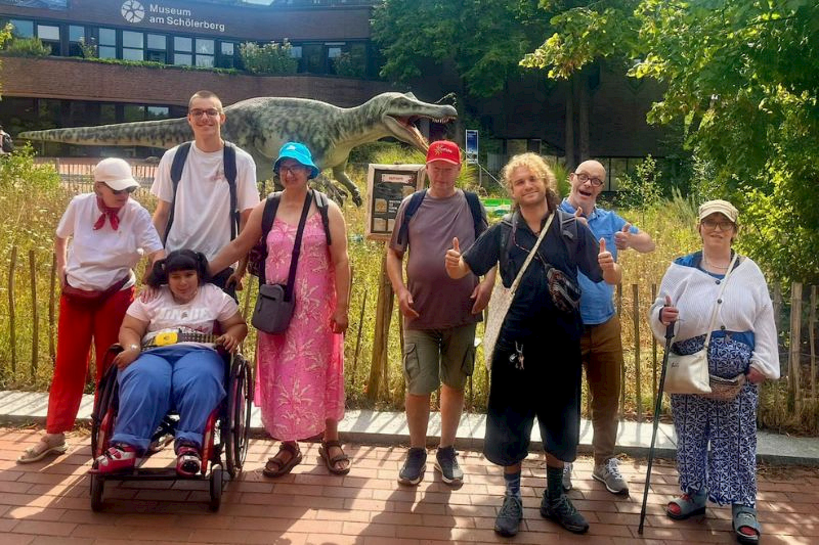 Das Bild zeigt Menschen aus den Archen in Gent und Tecklenburg, die im Naturkundemuseum Osnabrück vor einem künstlichen Dinosaurier stehen.
